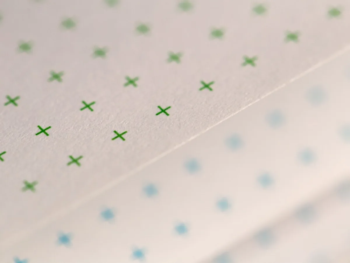 Close-up of two sheets of notebook paper side by side, one printed with a green cross grid and the other with a pale blue dot grid