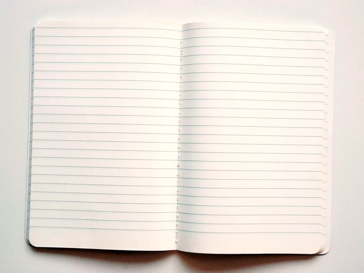 An open notebook showing two blank ruled pages in bright even light, the ruling faint and evenly spaced